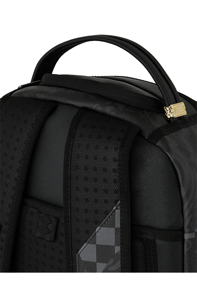 Close-up of a black backpack showing the top handle, padded shoulder straps, textured fabric panels, and a small gold zipper pull on a white background.