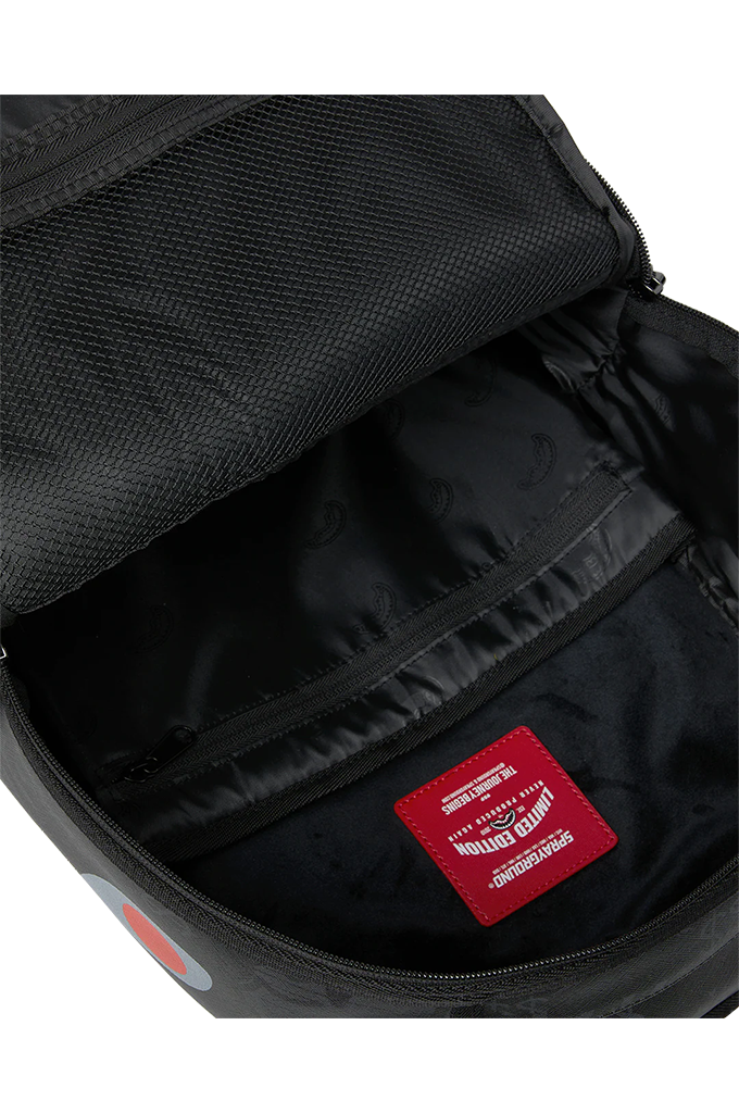 Close-up of the interior of a black backpack, showing a black mesh fabric lining, a zippered pocket, and a red brand patch with white text.