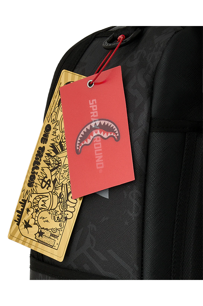 Close-up of a black backpack with attached red and gold Sprayground brand tags, showing the Shark logo and graffiti-style artwork on a white background.