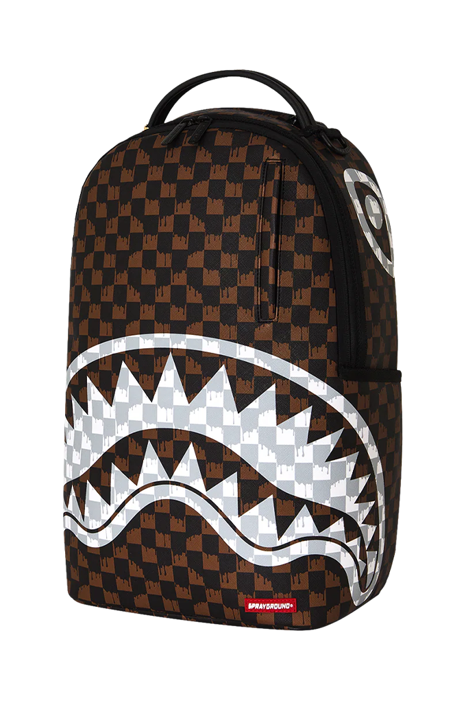A Sprayground Shark backpack featuring a brown and black checkered pattern, a large white shark mouth graphic across the front, and a small red Sprayground logo tag at the bottom right.