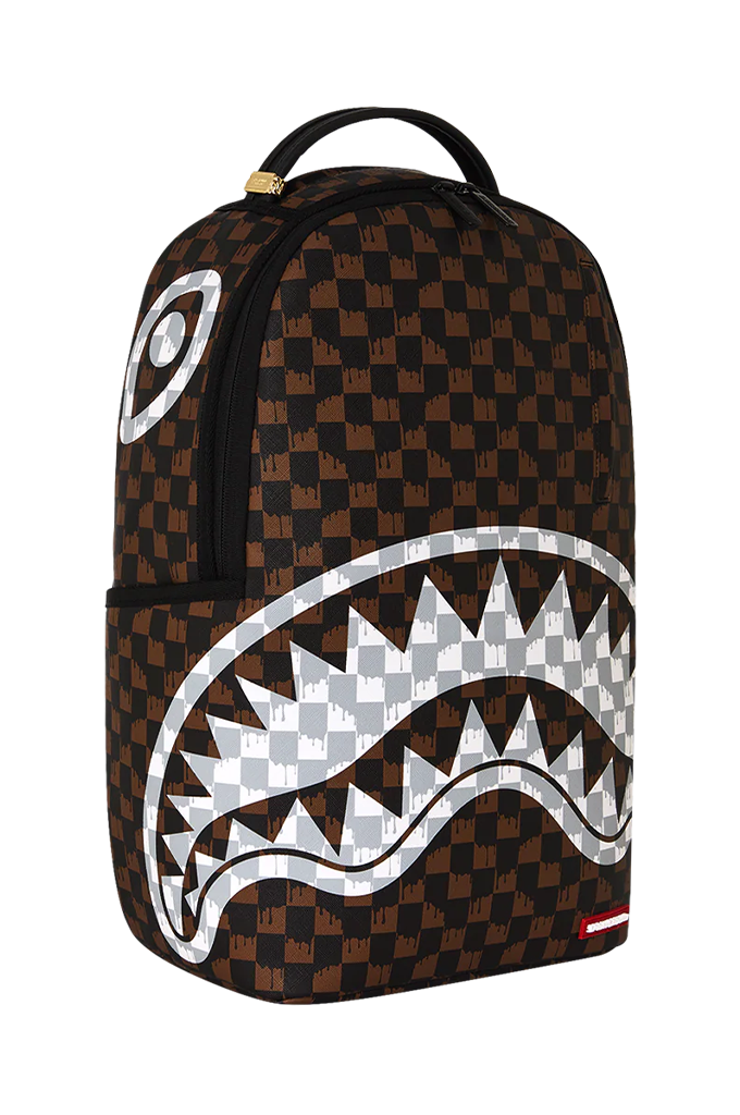 A Sprayground Shark backpack featuring a brown and black checkered pattern, a large white shark mouth graphic across the front, and a small red Sprayground logo tag at the bottom right.
