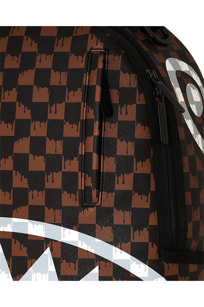 Close-up of a backpack or bag featuring a black and brown checkerboard pattern with a shark-mouth graphic in white at the bottom and a large white circular logo on the side.