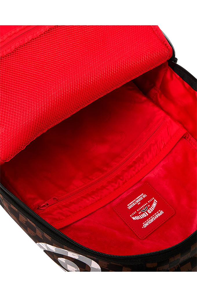 Close-up of an open backpack showing a bright red interior lining with a zip pocket and a visible SPRAYGROUND label patch.