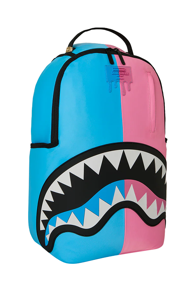 A Sprayground Shark backpack in a split blue and pink colorway, featuring a large shark mouth graphic with black, white, and pink details on the front.
