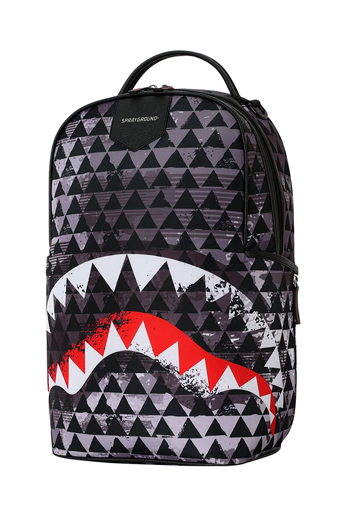 A Sprayground backpack featuring a black and gray geometric triangle pattern with a large shark mouth graphic in red, white, and black on the lower front pocket.