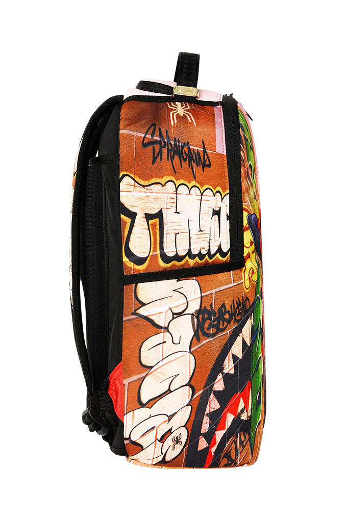 A backpack featuring a graffiti art print with the word 'THUG' in large white bubble letters, black spray-paint style text, a brick wall background, and a shark mouth graphic on the lower right. The backpack has black straps and trim, photographed against a plain white background.