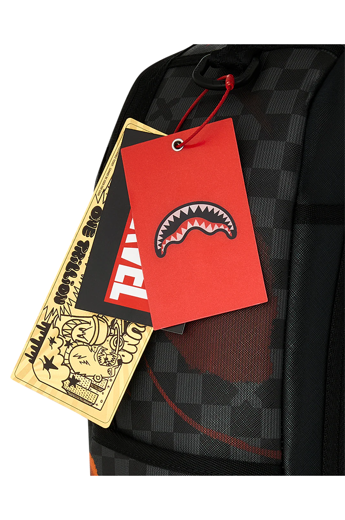 Close-up of a black checkered backpack with a red hanging tag featuring a shark-mouth logo, alongside a gold and black illustrated hangtag.