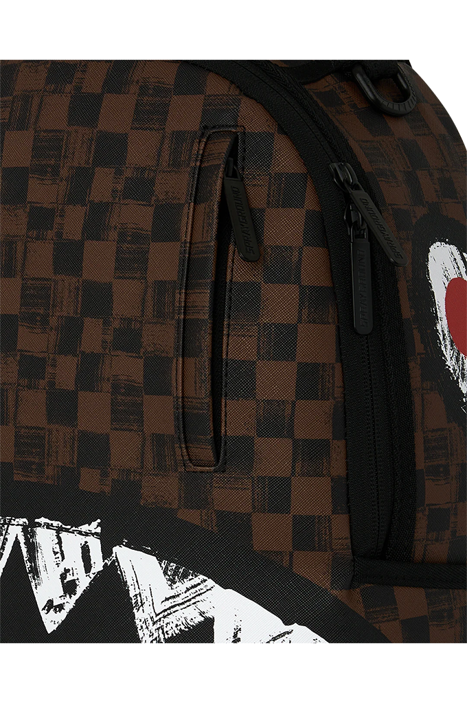 Close-up of a backpack featuring a brown and black checkerboard pattern, black zippers, and a partial white graphic with a red heart on the side.