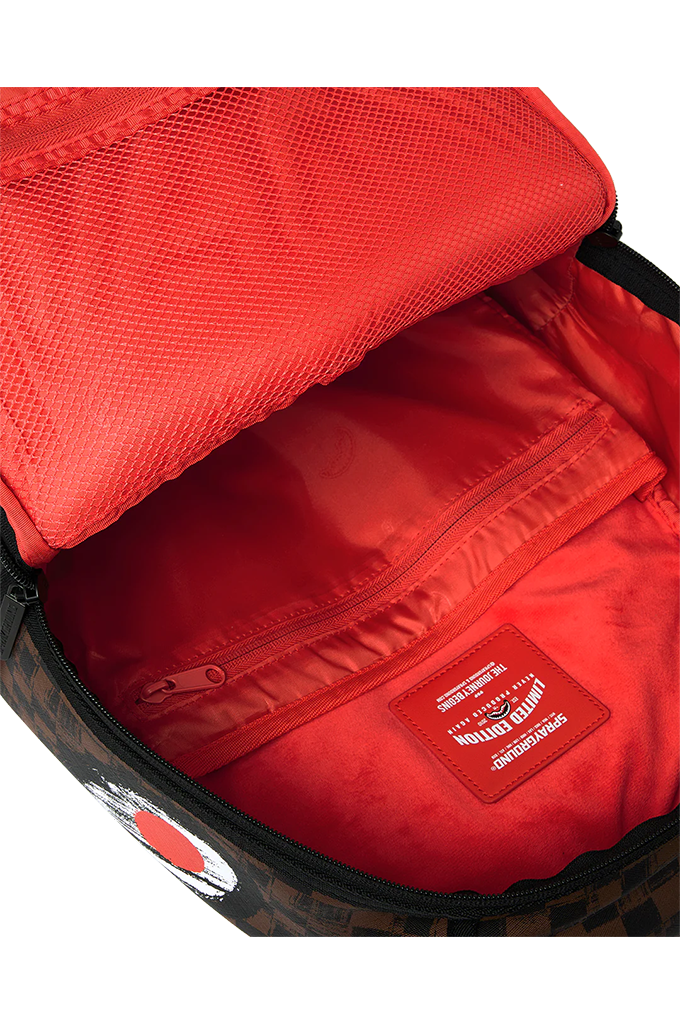 Close-up of the interior of a backpack showing a bright red mesh lining, zippered compartment, and a red brand patch with white text. The exterior edge shows a dark brown and black patterned fabric.