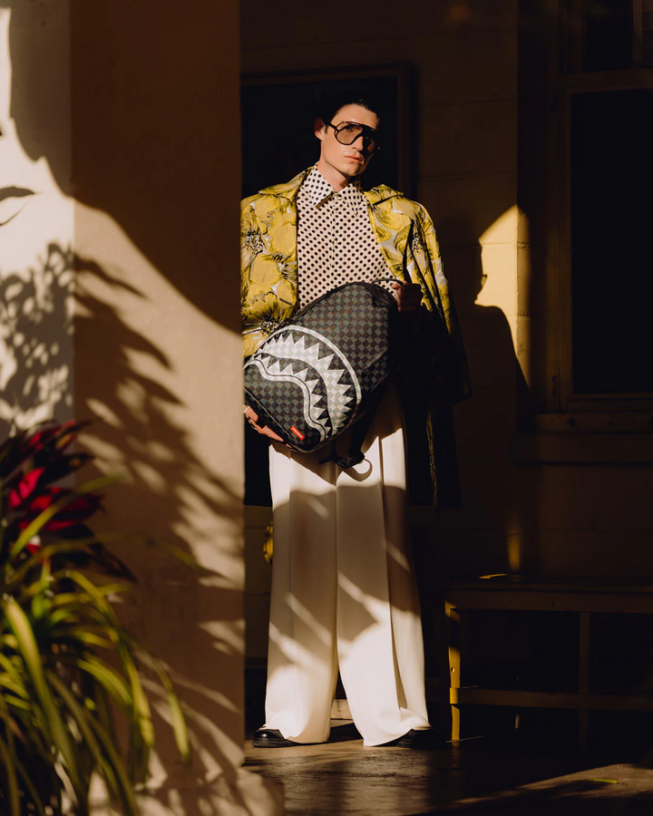 Person holding a patterned bag in a dimly lit room with shadows on the wall.