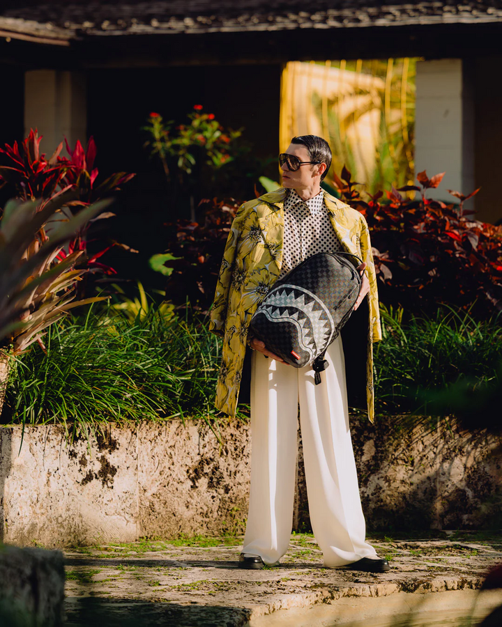 Person holding a black and gray patterned bag in a garden setting