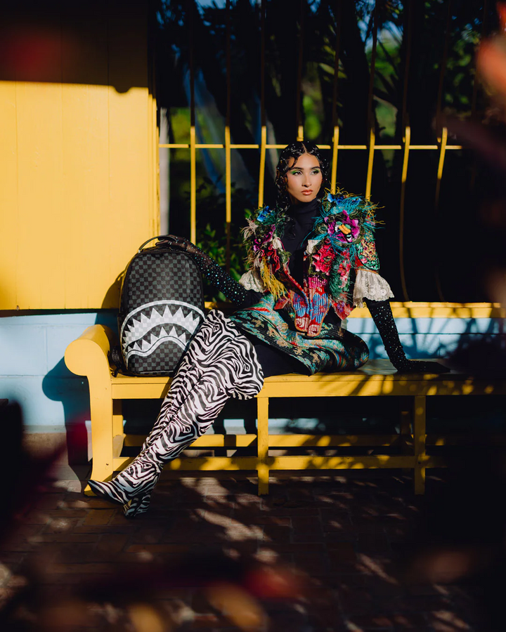 Person sitting on a yellow bench wearing a colorful outfit with a shark backpack.