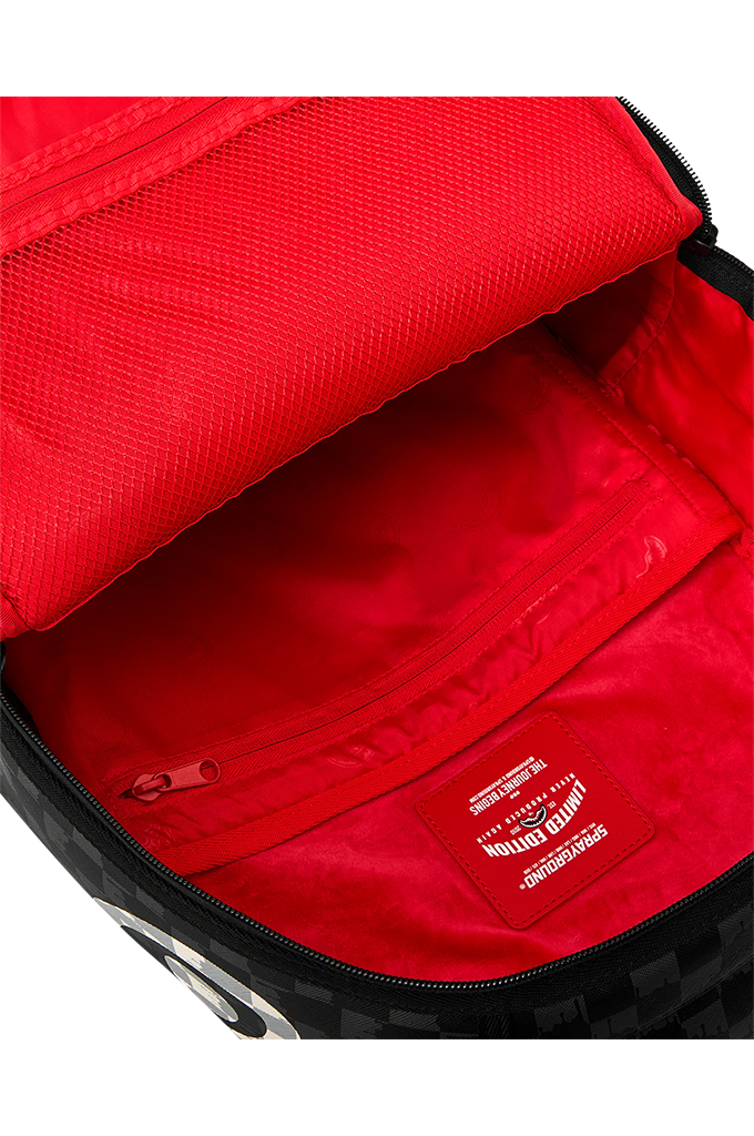 Close-up of the interior of a backpack showing a bright red nylon lining, zippered pocket, and a red brand patch. The exterior edge shows a black and white checkered pattern.