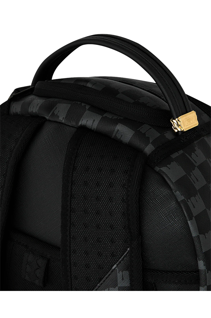 Close-up of a black backpack showing the top handle, padded shoulder strap, textured fabric, and a small gold-tone hardware accent against a white background.