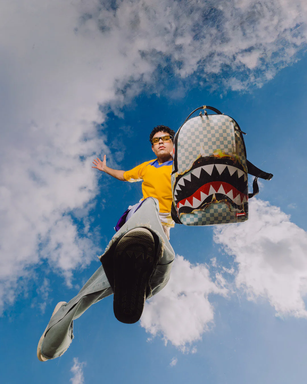Person with a shark-themed backpack against a blue sky with clouds