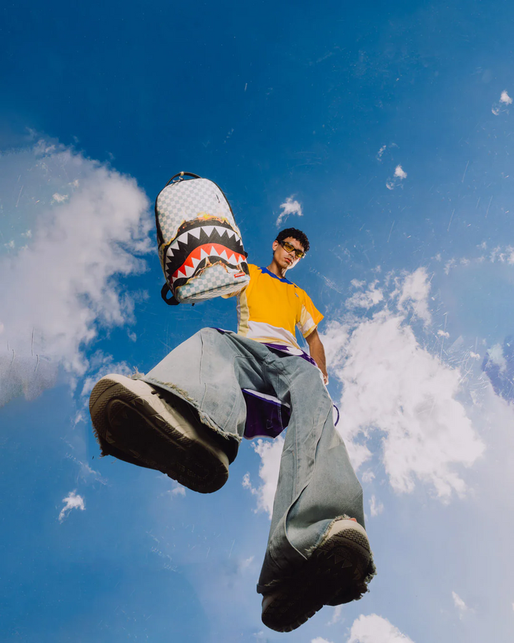 Person holding a shark-patterned bag against a blue sky with clouds