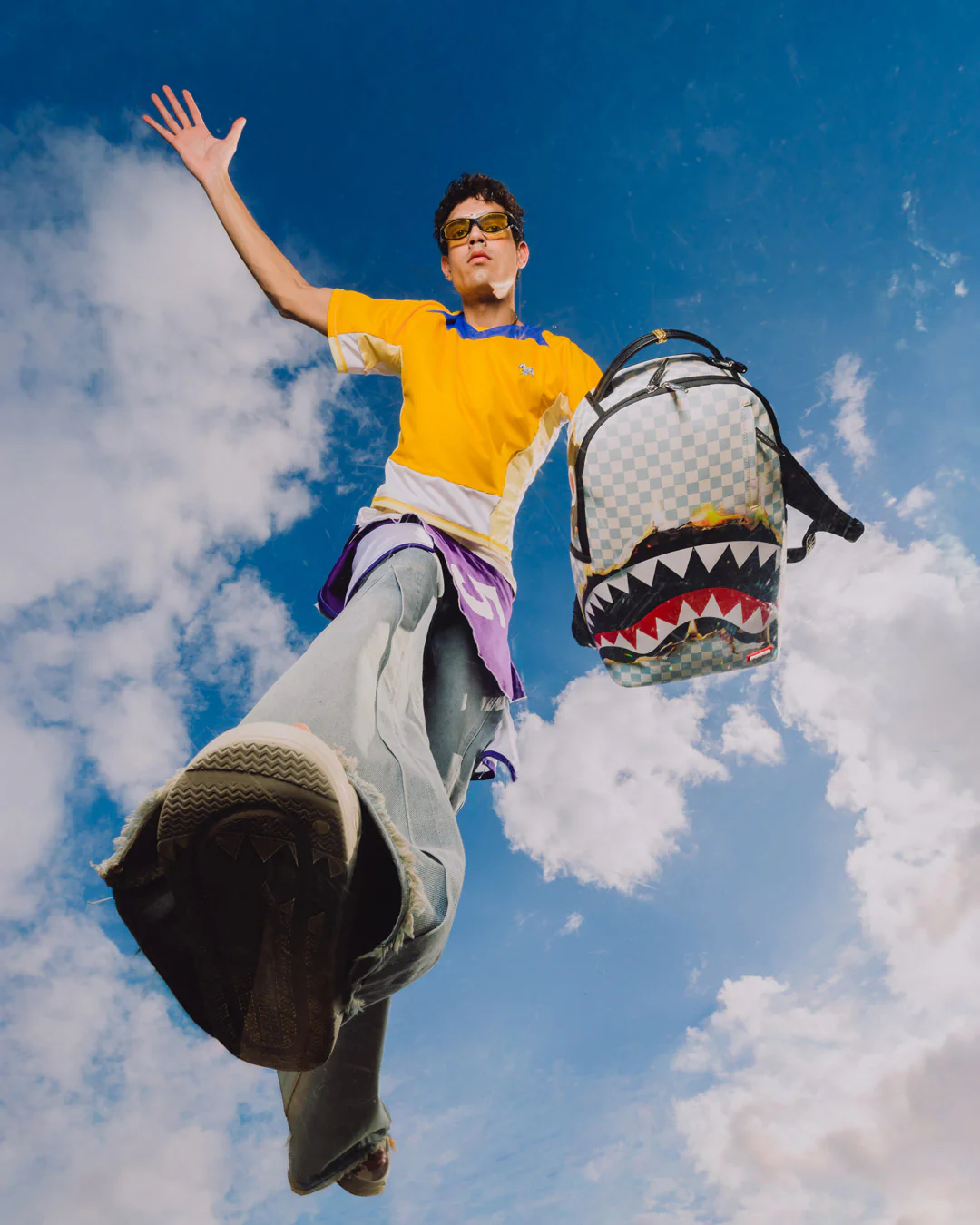 Person in yellow shirt with a shark-patterned backpack against a blue sky with clouds