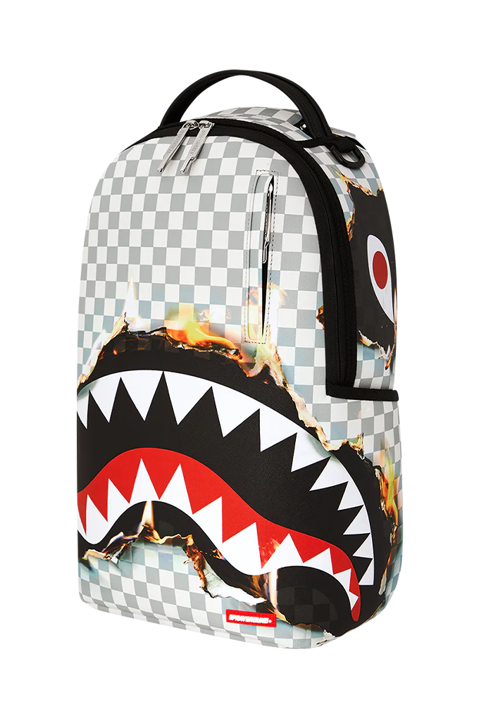 A Sprayground Shark backpack featuring a black and white checkered pattern, a large black shark mouth graphic with white, red, and black teeth, and a burning effect across the middle, shown on a plain white background.