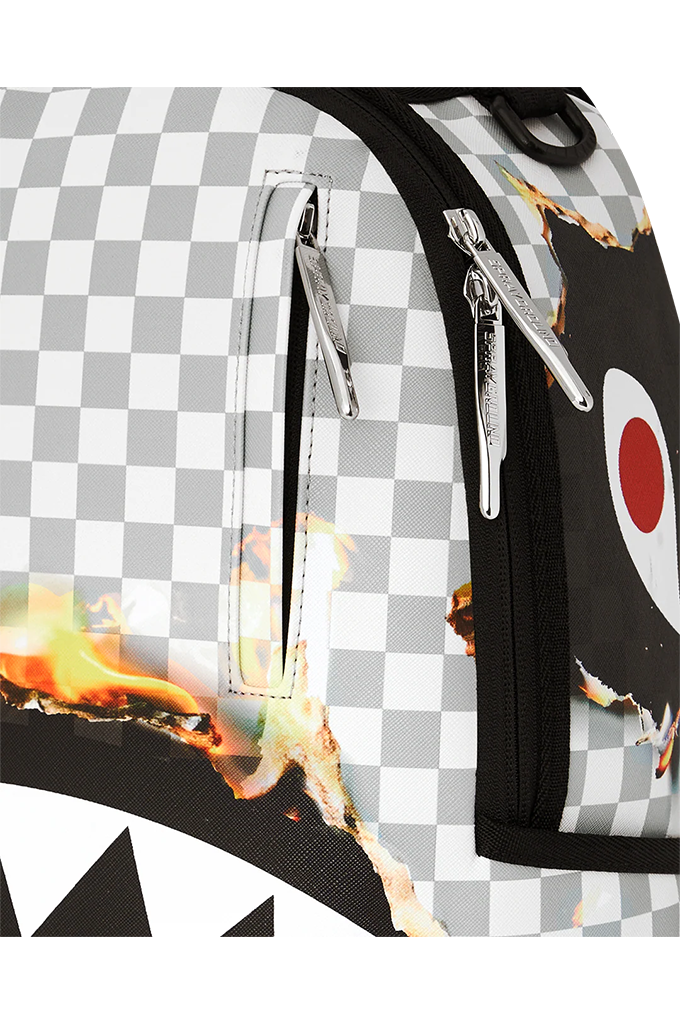 Close-up of a backpack or duffel bag featuring a gray and white checkerboard pattern, black trim, silver zippers, and flame graphics with a shark-face style eye motif.