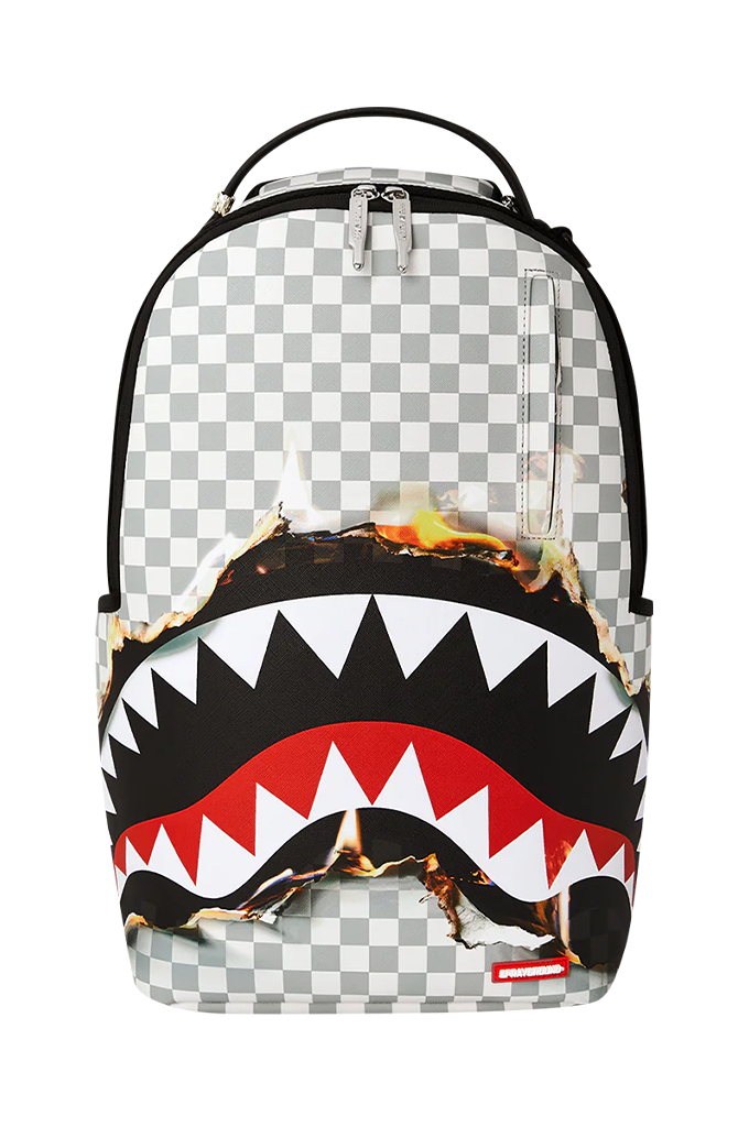 A Sprayground Shark backpack featuring a black and white checkered pattern, a large black shark mouth graphic with white, red, and black teeth, and a burning effect across the middle, shown on a plain white background.
