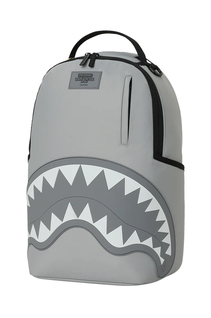 A gray Shark backpack with a black top handle, black zipper details, and a large shark mouth graphic on the front featuring white and dark gray teeth.