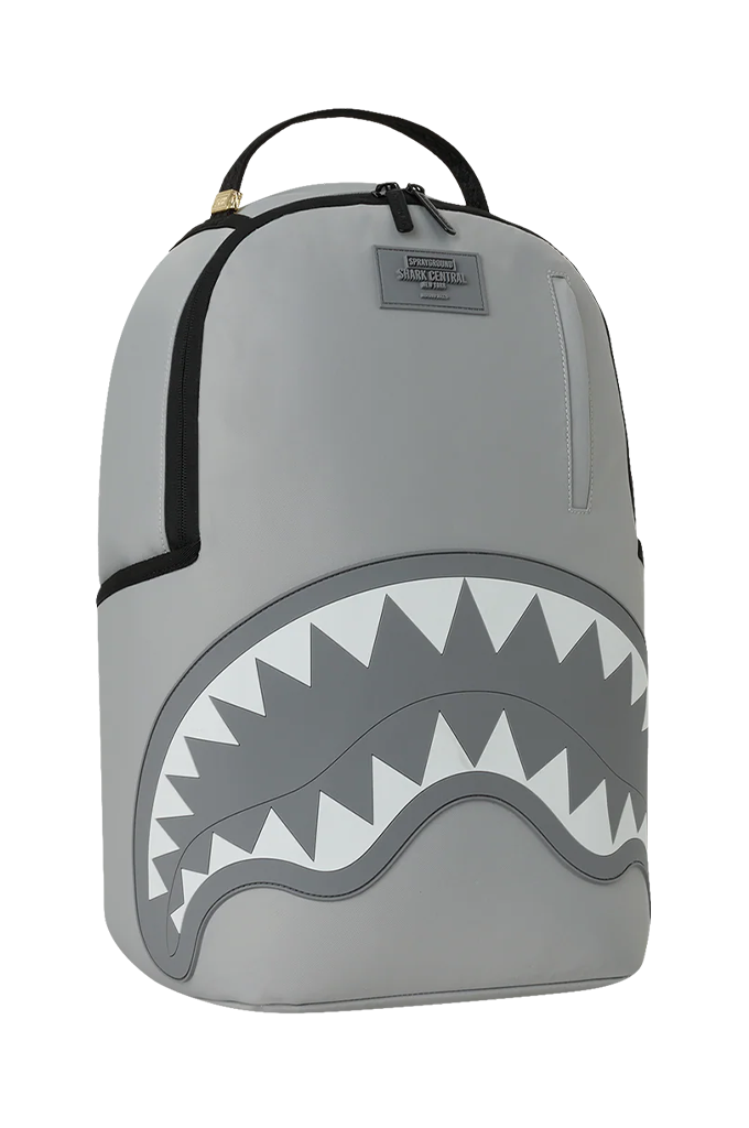A gray Shark backpack with a large shark mouth graphic on the front, black zipper details, and a top carry handle, shown against a plain white background.