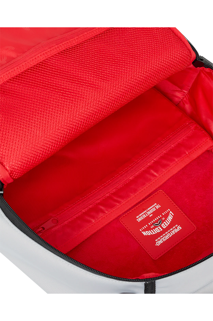 Close-up of the interior of a backpack showing a bright red mesh lining, zippered compartment, and a red interior label with white text.