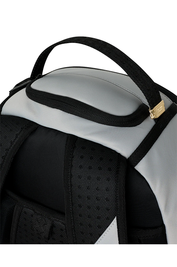 Close-up of a backpack showing the top handle, a zippered pocket, black mesh padding, and a small gold brand tag on a white background.