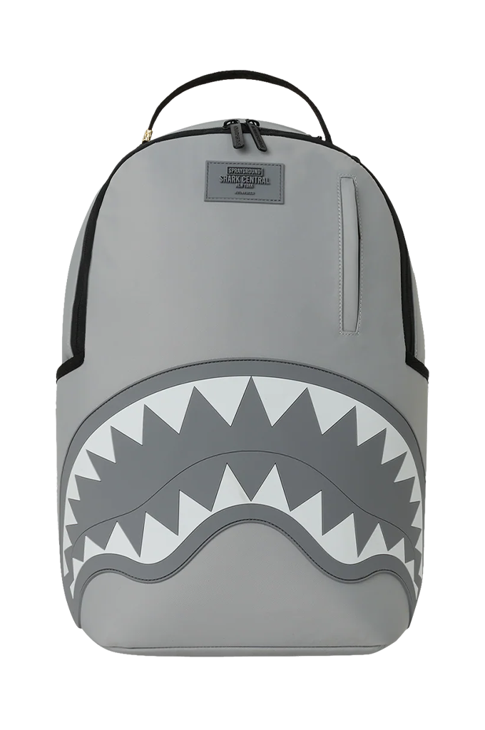 A gray Shark mouth backpack from Sprayground with a black top handle, black piping, and a large shark mouth graphic on the front in gray, white, and black. A small gray brand patch is visible near the top center.
