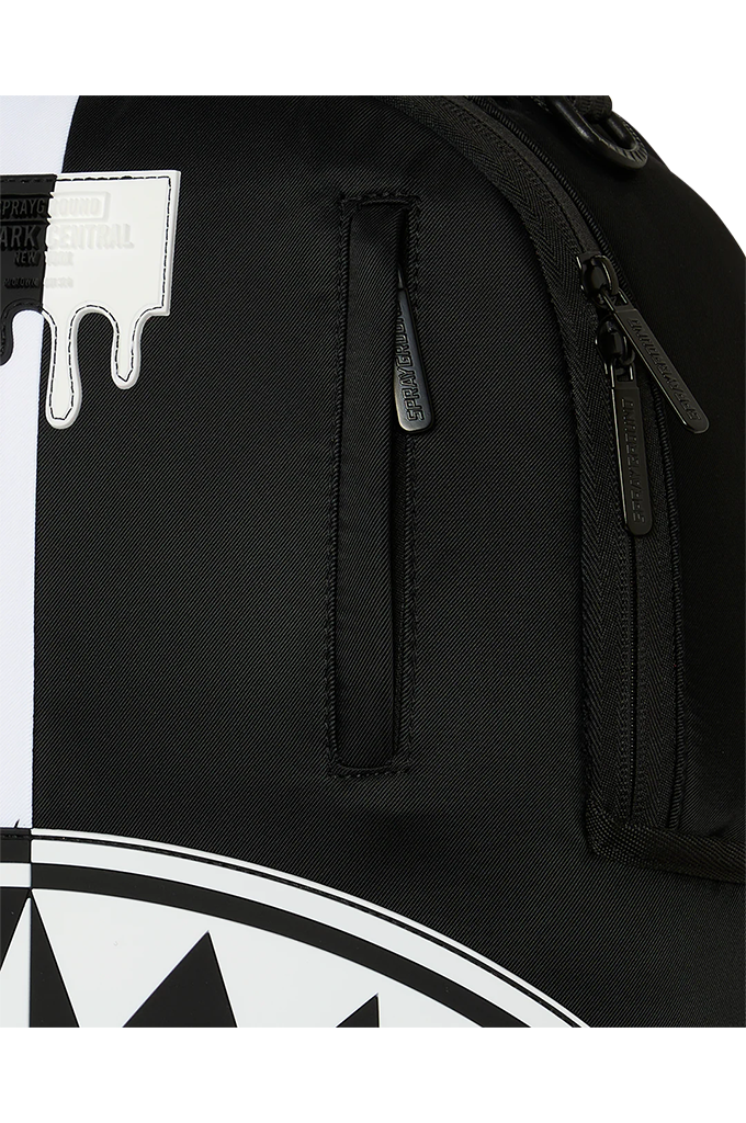 Close-up of a black backpack showing the side pocket, zipper details, and part of a white graphic print with a dripping paint motif.