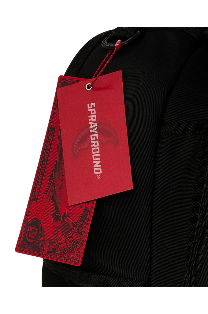 Close-up of a black backpack with a bright red hanging tag printed with the brand name 'SPRAYGROUND' in white.