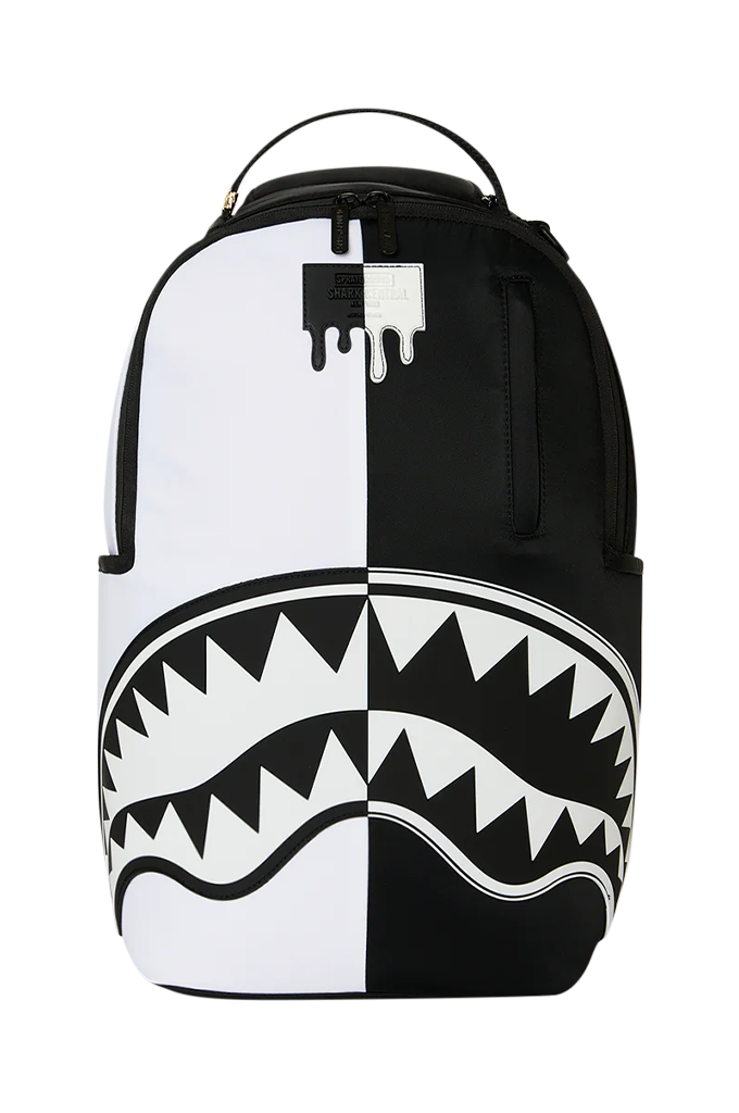 A black and white spray-paint style backpack featuring a shark mouth graphic across the lower half, with a top carry handle and zippered compartments.