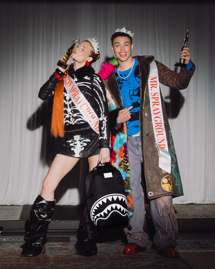 Two people in costume with 'Mr. Sprayground' and 'Miss Sprayground' sashes, posing on a stage.