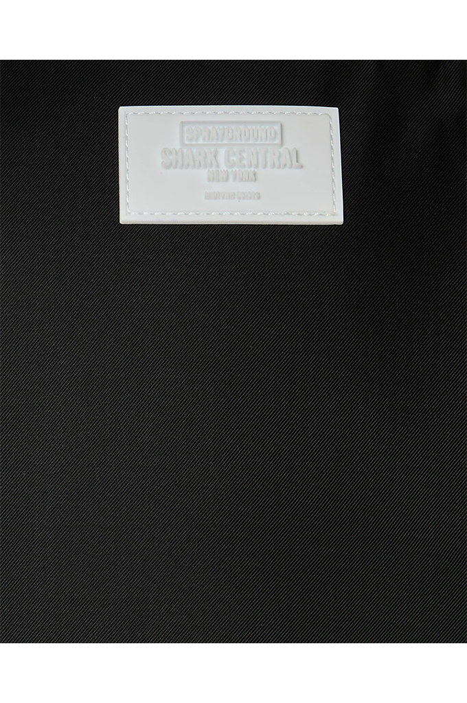 Close-up of a black textured fabric item with a white rectangular brand patch reading SHARK CENTRAL NEW YORK.
