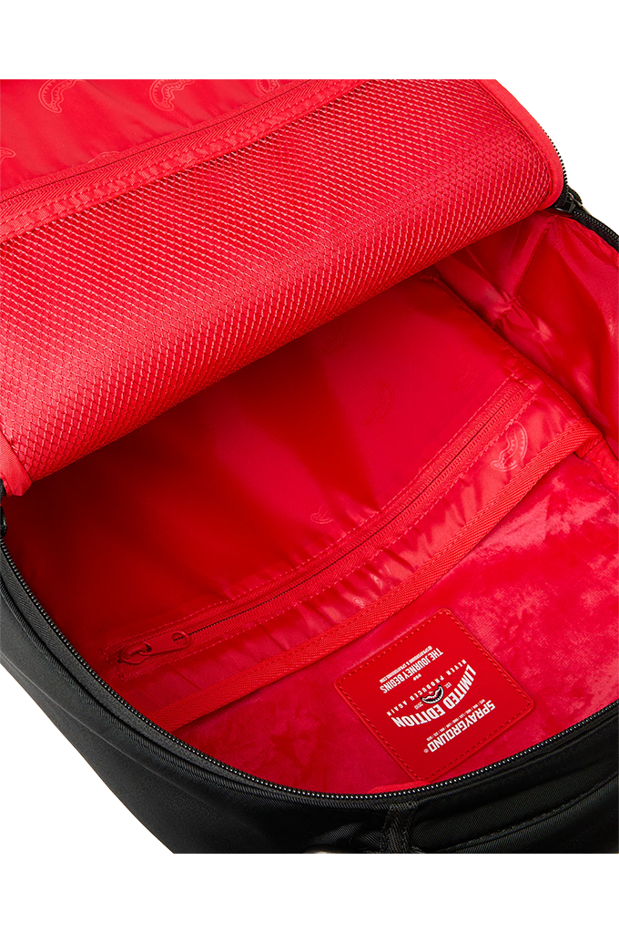 Close-up of the interior of a backpack showing a bright red nylon lining, zippered compartments, and a red brand patch with white text.
