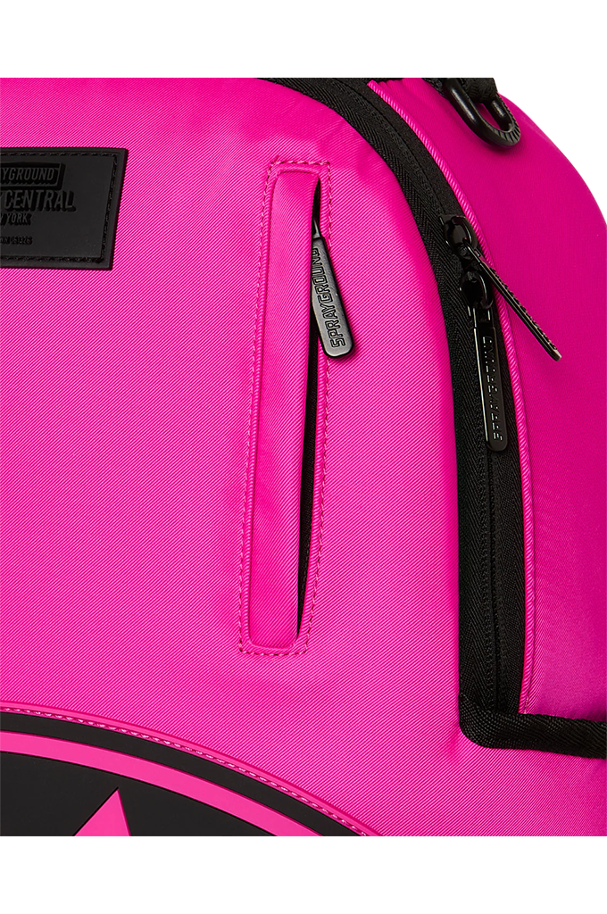 Close-up of a bright pink backpack showing a vertical zippered pocket with a black zipper pull, a black brand patch on the upper left, and black zipper tracks.