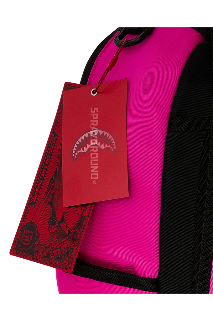 Close-up of a bright pink and black backpack with a red hangtag featuring the SPRAYGROUND shark logo.