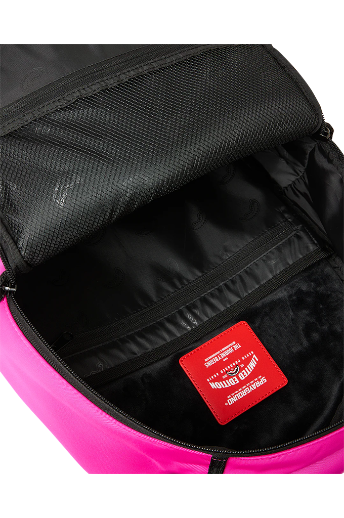 Close-up of the open interior of a backpack, showing a black mesh-lined compartment, black zipper, and a red rectangular brand patch on the lining. The backpack body is bright pink at the bottom edge.