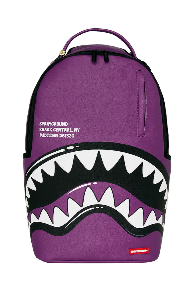 A purple Sprayground Shark Central backpack featuring a large shark mouth graphic with white teeth and black outlines on the front, with Sprayground branding printed on the side.