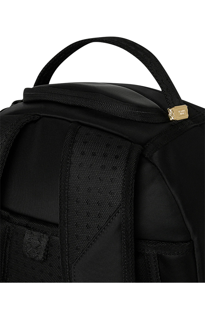 Close-up of a black backpack showing the top handle, a zippered compartment with a small gold-tone metal accent, and textured fabric panels on a plain white background.