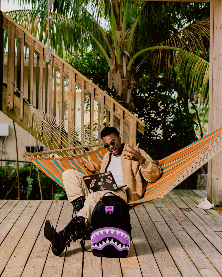 Man sitting in a hammock on a wooden deck with palm trees in the background