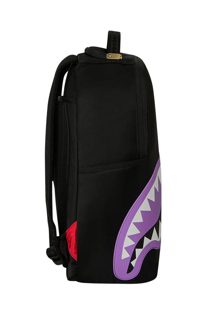 A black backpack featuring a large purple shark mouth graphic with white teeth on the lower right side, and a small red accent on the lower left side.
