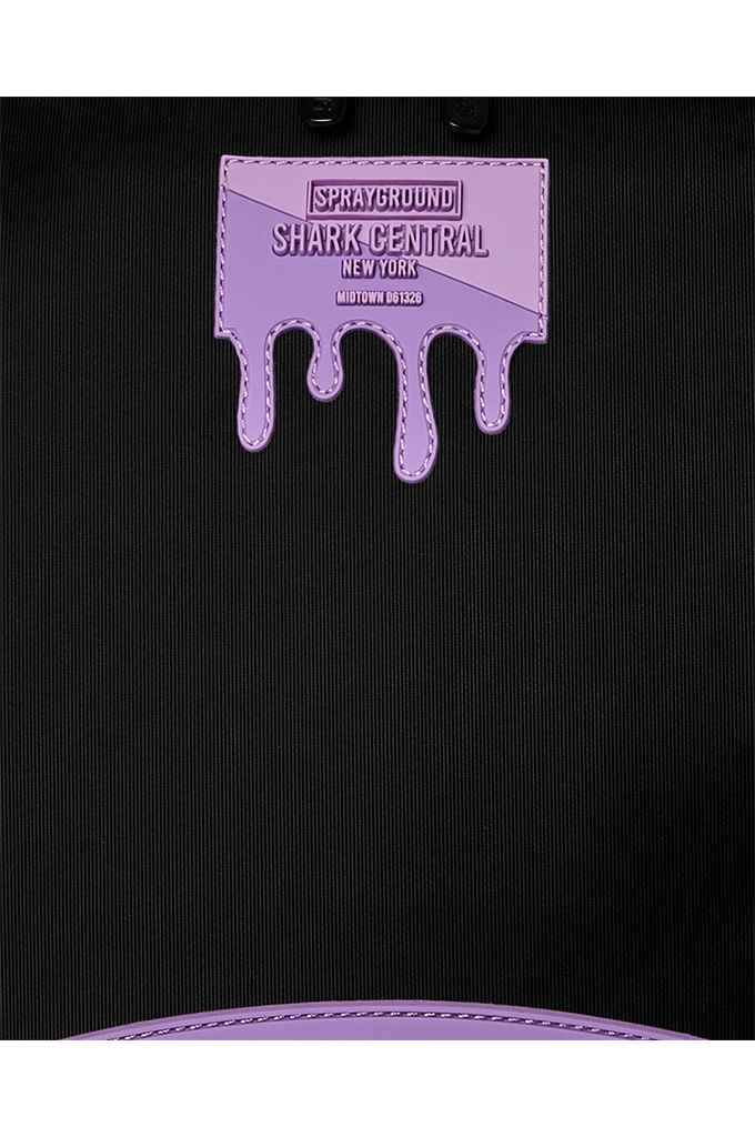 Close-up of a black ribbed fabric item featuring a lavender purple dripping patch with the text 'SPRAYGROUND SHARK-CENTRAL NEW YORK' and a matching purple stitched edge at the bottom.