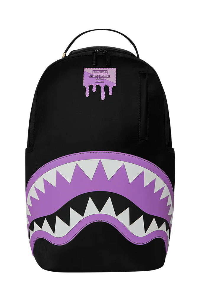 A black backpack featuring a large purple and white shark mouth graphic on the front, with a small purple dripping tag near the top.