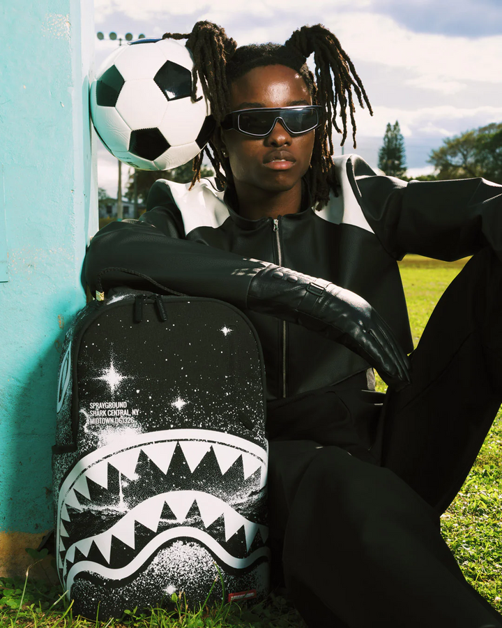 Person holding a soccer ball with a shark design backpack outdoors
