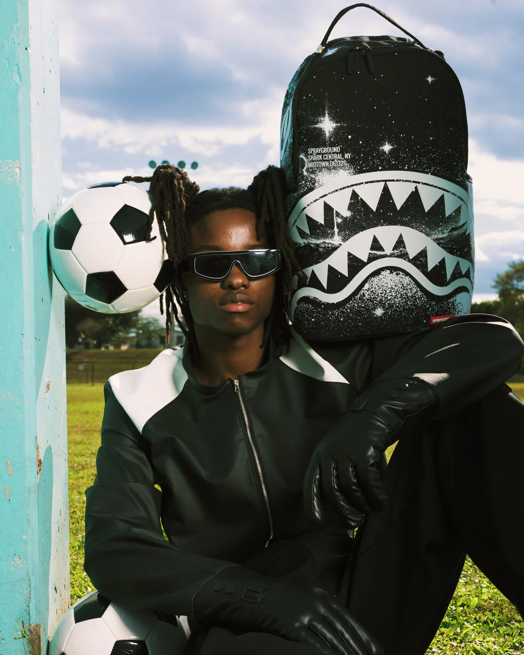 Person holding a shark-patterned bag and soccer ball on a grassy field