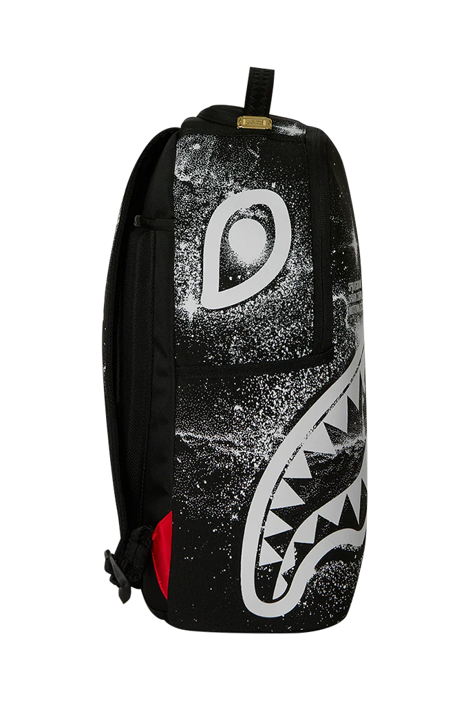 A black backpack featuring a large white shark face graphic on the front, with a small red accent on the lower side and a gold brand tag near the top handle.