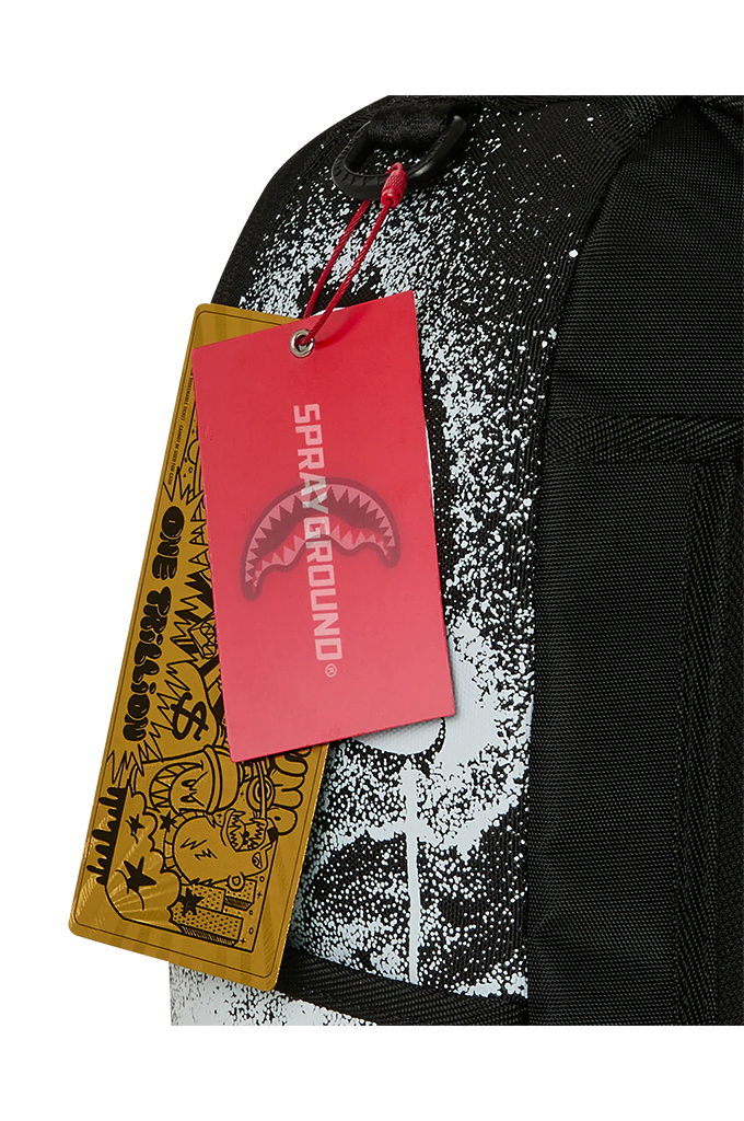 Close-up of a black backpack with a white and black graffiti-style print, featuring a red Sharkrayne 'SPRAYGROUND' hangtag and a yellow tag attached.