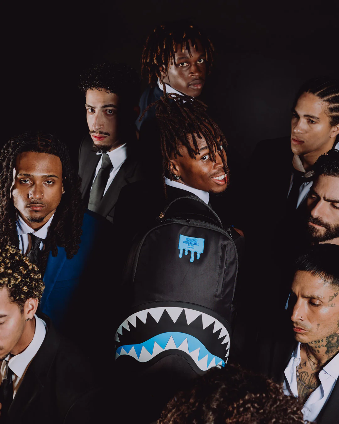 Group of men in formal attire with a person wearing a shark-themed backpack.