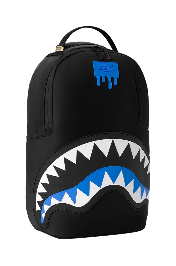 A black Sprayground backpack featuring the iconic shark mouth graphic with white and blue details, and a blue Spray-R logo patch on the upper front.